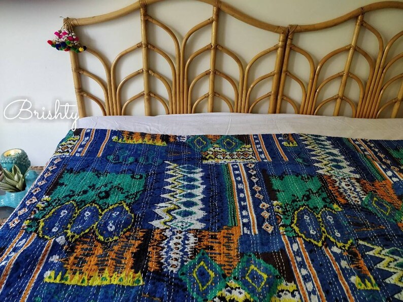 May include: A blue and green kantha quilt with a geometric pattern. The quilt is on a bed with a bamboo headboard.