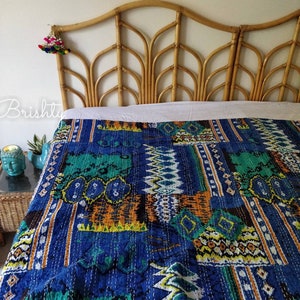 May include: A blue and green kantha quilt with a geometric pattern is draped over a rattan headboard. The quilt is made of cotton and has a hand-stitched design.