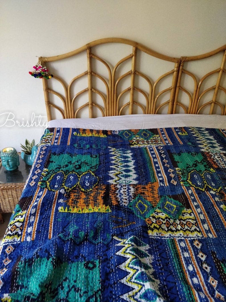 May include: A blue and green kantha quilt with a geometric pattern is draped over a rattan headboard. The quilt is made of cotton and has a hand-stitched design.