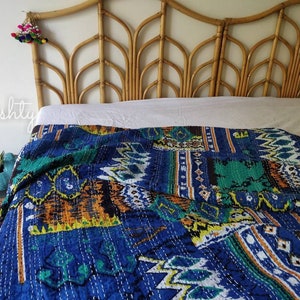 May include: A blue and green kantha quilt with a geometric pattern is draped over a bed with a light brown wicker headboard.