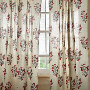 May include: A pair of cream-coloured curtains with a red and grey floral print. The curtains are hanging in a window and are letting in natural light.