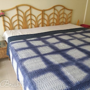 May include: A blue and white kantha quilt with a grid pattern. The quilt is on a bed with a wicker headboard.