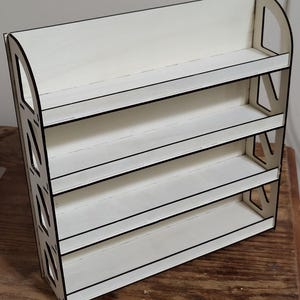 May include: White wooden shelf unit with four shelves. The shelves have black edges and are designed to hold small items.