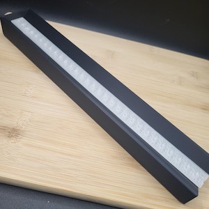May include: A black rectangular tray with a white, textured strip running down the center.