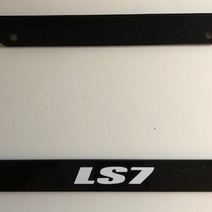 Puede incluir: Marco de matrícula de plástico negro con letras blancas que dicen "LS7".