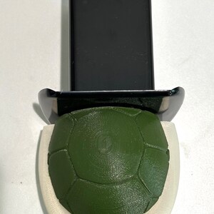 Könnte beinhalten: Eine grüne Schildkrötenpanzer mit einem weißen Rand, befestigt an einer schwarzen Plastikbasis.