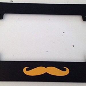 May include: Black motorcycle number plate frame with a yellow moustache design.