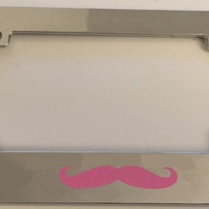 May include: A chrome licence plate frame with a pink moustache design.