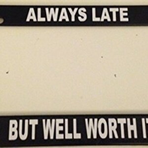 May include: Black plastic license plate frame with white text that reads "Always Late But Well Worth It".