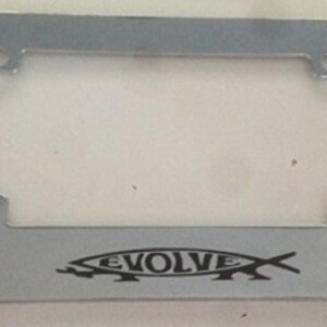 May include: A silver metal license plate frame with a black fish graphic and the word "EVOLVE" printed on it.