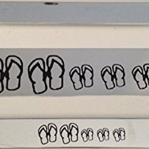 Könnte beinhalten: Ein silberner Kennzeichenrahmen mit einem schwarzen Umriss von Flip-Flops, die darauf gedruckt sind. Die Flip-Flops sind in verschiedenen Größen und in einer Reihe angeordnet.