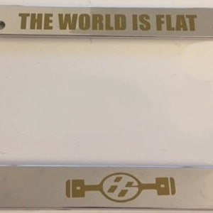 Może przedstawiać: Chromowana ramka na tablicę rejestracyjną z złotym napisem "THE WORLD IS FLAT". Na dole ramki znajduje się złote logo części samochodowej.