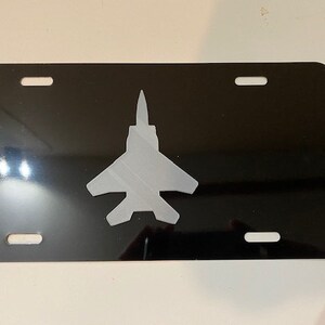 May include: Black metal license plate with a silver silhouette of a fighter jet.
