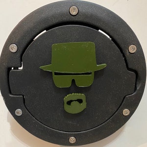 Può includere: Un tappo del serbatoio rotondo nero con una silhouette verde di un uomo con cappello, occhiali da sole e baffi.