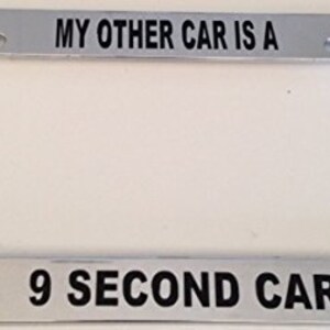 May include: A silver license plate frame with the text "My other car is a 9 second car".