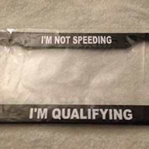 May include: Black license plate frame with white text that reads "I'm not speeding I'm qualifying".