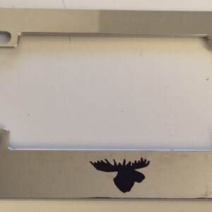 Puede incluir: Marco de matrícula de motocicleta cromado con una silueta de alce negra.