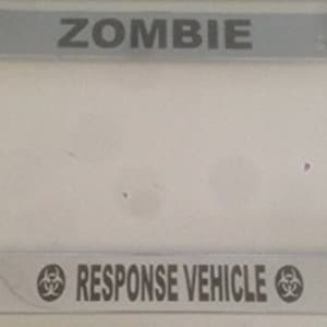 May include: A silver metal license plate frame with the text "ZOMBIE RESPONSE VEHICLE" and a biohazard symbol on either side.