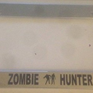 May include: A silver license plate frame with the text "ZOMBIE HUNTER" and a graphic of two stick figures.