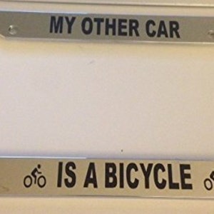Puede incluir: Un marco de matrícula plateado con el texto "MY OTHER CAR IS A BICYCLE" y un icono de bicicleta a cada lado.