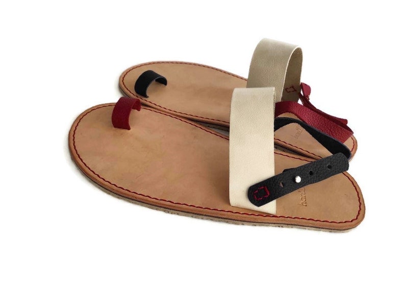 Puede incluir: Dos pares de sandalias de cuero con correas ajustables. Las sandalias tienen un bucle para el dedo del pie y una correa trasera. Las correas son de diferentes colores, incluyendo negro, rojo y beige.
