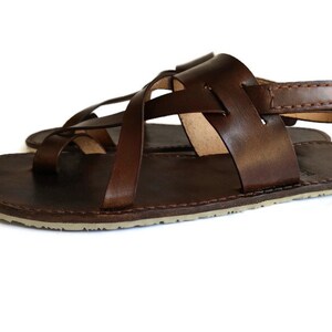 Op de afbeelding: Bruine leren sandalen met een gekruist bandontwerp en een achterband. De sandalen hebben een platte zool.