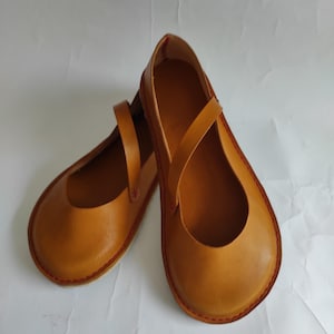 Pode incluir: Um par de sapatos de couro castanho com costuras vermelhas. Os sapatos t&ecirc;m um design simples com uma &uacute;nica tira na parte superior.