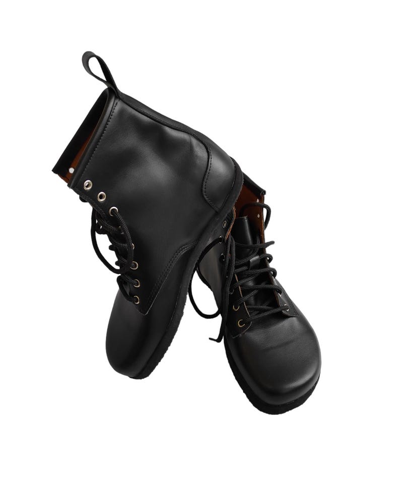 Puede incluir: Un par de botines de cuero negro con dise&ntilde;o de cordones. Las botas tienen punta redondeada y una presilla en la parte trasera. Las botas se muestran sobre un fondo blanco.
