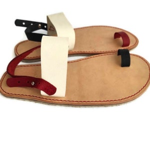 Puede incluir: Un par de sandalias de cuero con un bucle para el dedo del pie y una correa para el tobillo. Las sandalias est&aacute;n hechas de cuero marr&oacute;n con detalles en rojo, blanco y negro.