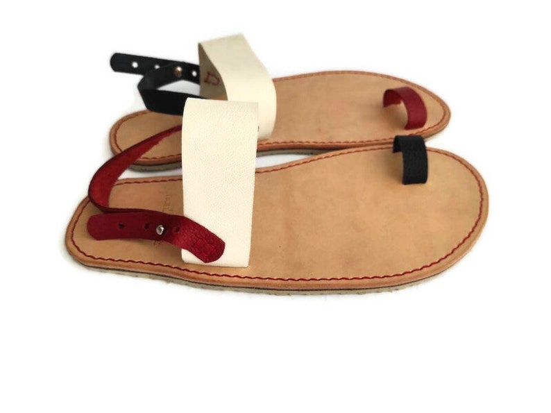 Puede incluir: Un par de sandalias de cuero con un bucle para el dedo del pie y una correa para el tobillo. Las sandalias est&aacute;n hechas de cuero marr&oacute;n con detalles en rojo, blanco y negro.