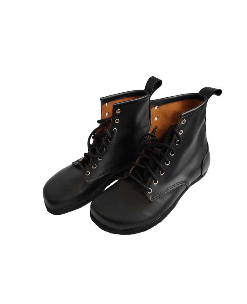 Puede incluir: Un par de botas de cuero negro con dise&ntilde;o de cordones. Las botas tienen punta redondeada y una leng&uuml;eta en la parte trasera. El forro interior es de color marr&oacute;n claro. Las botas se muestran sobre un fondo blanco.