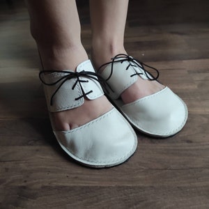 Puede incluir: Sandalias de cuero blanco con cordones negros. Las sandalias tienen un dise&ntilde;o recortado y un dedo cerrado.