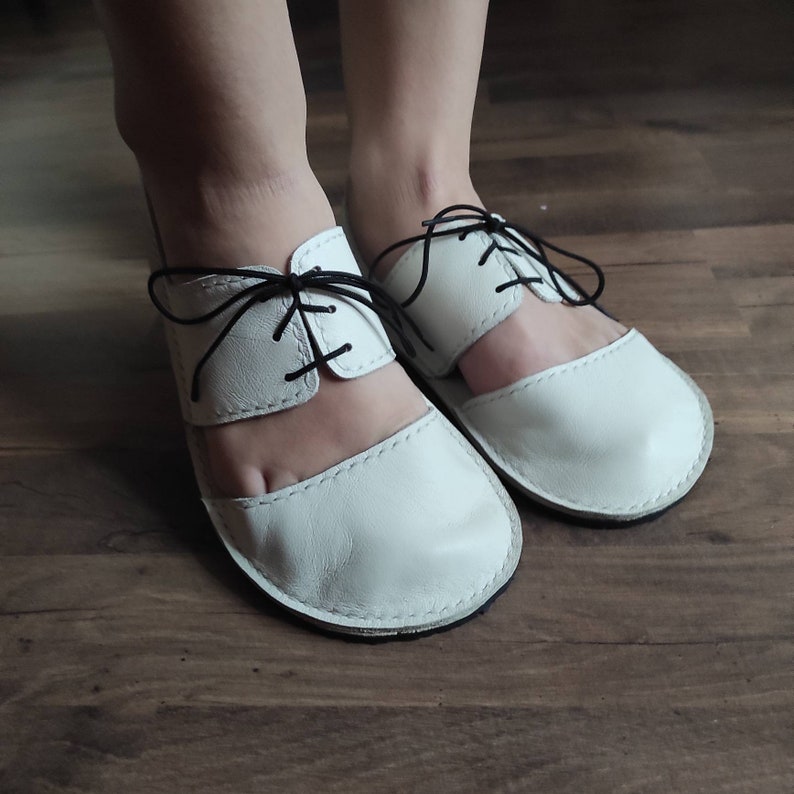 Puede incluir: Sandalias de cuero blanco con cordones negros. Las sandalias tienen un dise&ntilde;o recortado y un dedo cerrado.