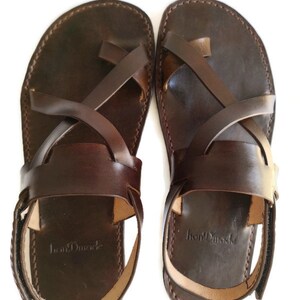 Op de afbeelding: Een paar bruine leren sandalen met gekruiste banden en een enkelband. De sandalen hebben een eenvoudig ontwerp en zijn gemaakt van hoogwaardig leer. De merknaam "IronMade" is zichtbaar op de zool van de sandalen.