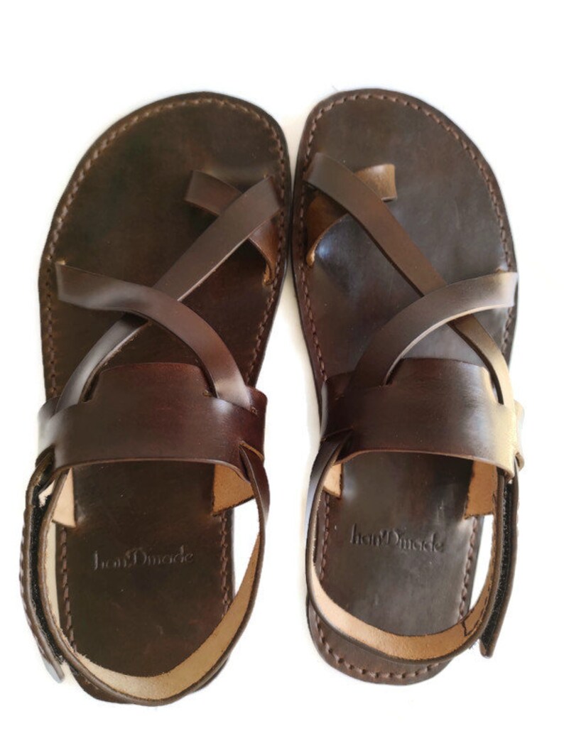 Op de afbeelding: Een paar bruine leren sandalen met gekruiste banden en een enkelband. De sandalen hebben een eenvoudig ontwerp en zijn gemaakt van hoogwaardig leer. De merknaam "IronMade" is zichtbaar op de zool van de sandalen.