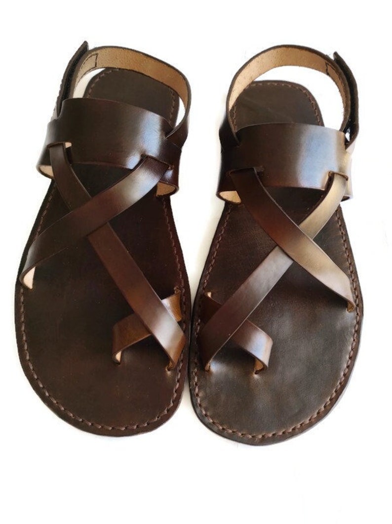 Op de afbeelding: Een paar bruine leren sandalen met gekruiste banden. De sandalen hebben een eenvoudig ontwerp en zijn gemaakt van hoogwaardig leer.