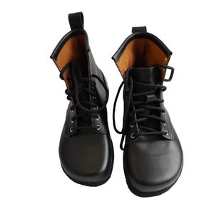 Puede incluir: Un par de botas de cuero negro con cordones. Las botas tienen una puntera redondeada y una leng&uuml;eta en la parte trasera. El interior es de color marr&oacute;n claro. Las botas se muestran sobre un fondo blanco.