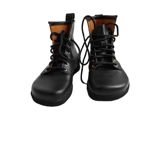 Puede incluir: Un par de botas de cuero negro con cordones negros. Las botas tienen una puntera redondeada y un interior marr&oacute;n. Los cordones est&aacute;n atados en forma de cruz. Las botas est&aacute;n sobre un fondo blanco.