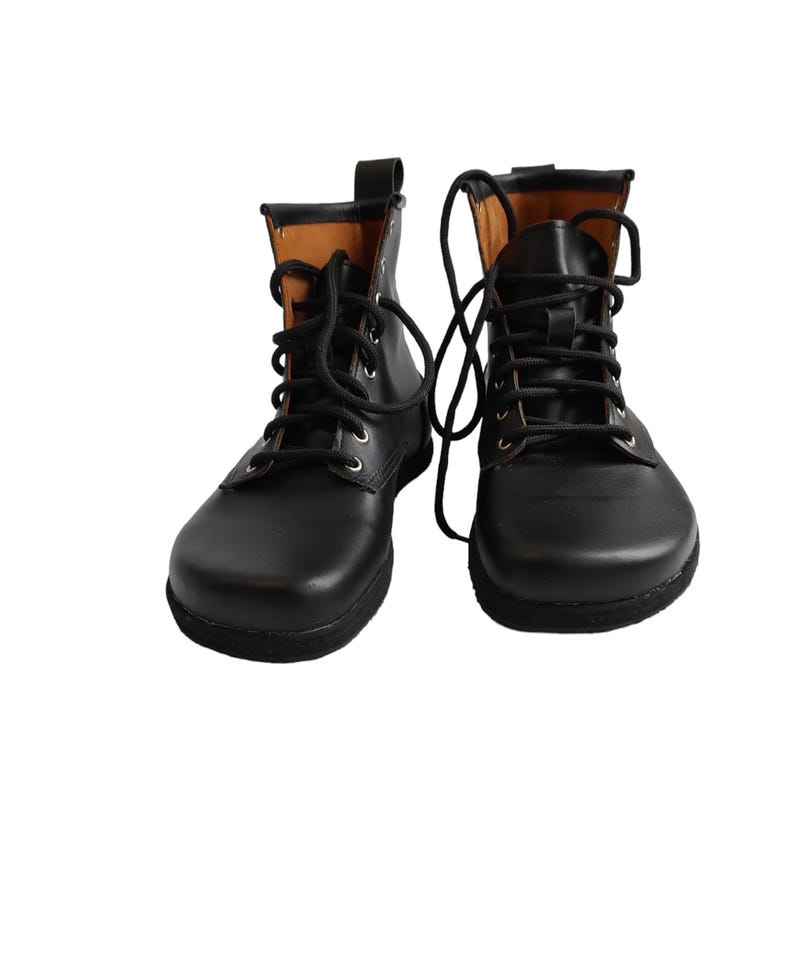 Puede incluir: Un par de botas de cuero negro con cordones negros. Las botas tienen una puntera redondeada y un interior marr&oacute;n. Los cordones est&aacute;n atados en forma de cruz. Las botas est&aacute;n sobre un fondo blanco.