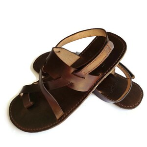 Op de afbeelding: Bruine leren sandalen met een gekruist bandontwerp. De sandalen hebben een open teen en een gespsluiting.