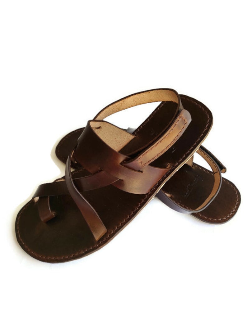 Op de afbeelding: Bruine leren sandalen met een gekruist bandontwerp. De sandalen hebben een open teen en een gespsluiting.