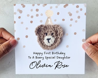 May include: A white card with brown confetti and a crocheted brown bear wearing a white and brown party hat with the number 1 on it. The card says "Happy First Birthday To A Beary Special Daughter Olivia Rose".