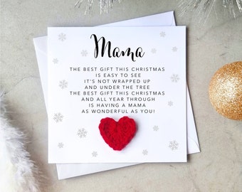 May include: A white Christmas card with the word "Mama" in cursive script. The card includes a red heart and a poem about a mother. Silver snowflake accents and a gold ornament are visible.