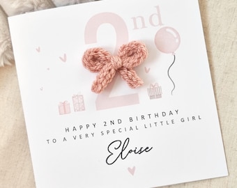 May include: A pink and white birthday card with a pink knitted bow and the text "Happy 2nd Birthday to a very special little girl Eloise".