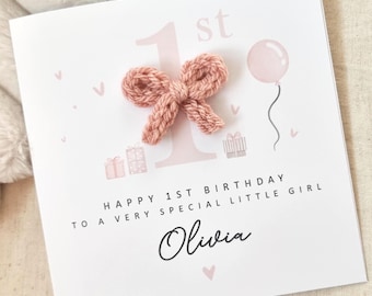 Può includere: Un biglietto di compleanno rosa e bianco con un fiocco di lana, un palloncino rosa e il testo "Happy 1st Birthday to a very special little girl Olivia".