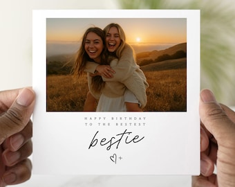 May include: A white greeting card with a photograph of two smiling people embracing in a field at sunset. The card reads "Happy Birthday to the Bestest" and "bestie" with a heart symbol.