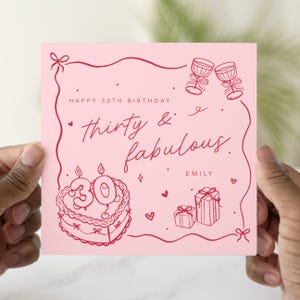 May include: A pink birthday card with red line art. The card says "Happy 30th Birthday, thirty & fabulous, Emily." The card features illustrations of a cake with candles, two wine glasses, and wrapped gifts.
