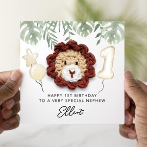 May include: A white card with a crocheted lion head, a white balloon with the number 1, and green leaves. The card says "Happy 1st Birthday to a very special nephew Elliot".