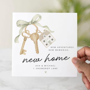Pu&ograve; includere: Una carta bianca con un'illustrazione ad acquerello di chiavi e un ciondolo a forma di casa, legati con un nastro verde. Le parole "new home" sono scritte in corsivo, con "New adventures, new memories" sopra. Nomi e indirizzo sotto.