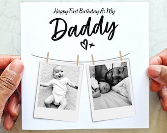 May include: A white greeting card with the text "Happy First Birthday As My Daddy" and two black and white photos. The photos are attached to a string with small clothespins. One photo shows a baby, the other shows a father and baby.